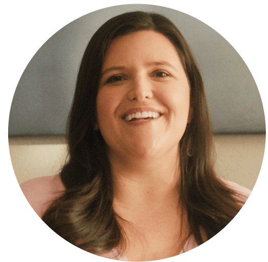 Smiling woman with long dark hair wearing a light pink top, framed in a circular coral background. Represents warmth, encouragement, and Noom’s supportive wellness community.